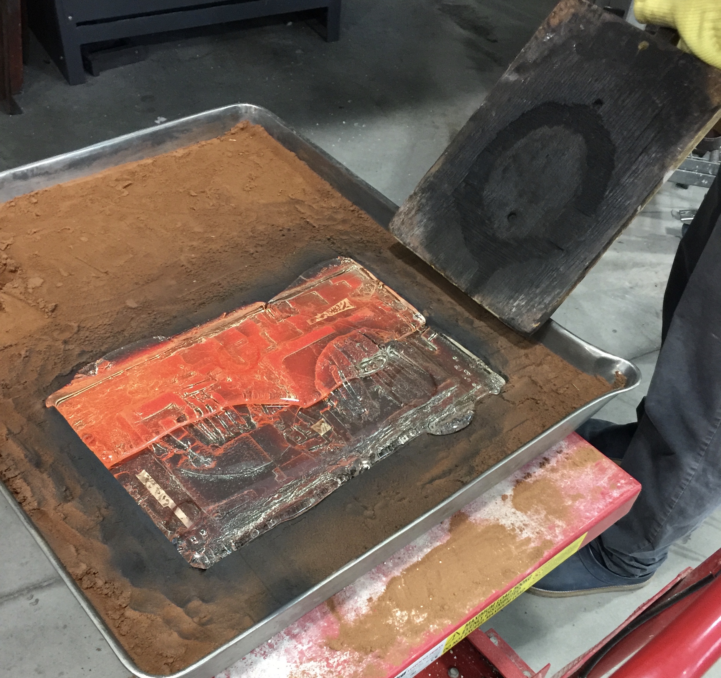 Glass being poured into sand cast which is a large patted down sand pit